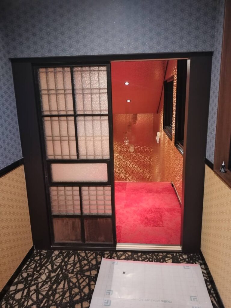麻の葉柄のクロスの壁に納めた格子の引き戸と、その先の赤いお部屋